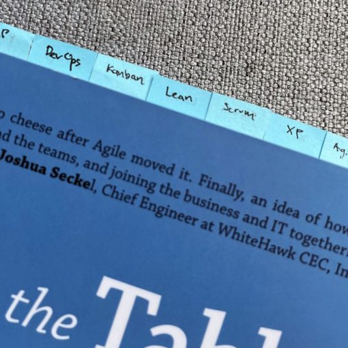 A photo of Lucy's copy of A Seat at the Table: IT Leadership in the Age of Agility, by Mark Schwartz. Only the upper part of the book is visible, and there are seven little blue tabs sticking out of the top of the book, labeled as follows: P2P, DevOps, Kanban, Lean, Scrum, XP, and Agile.